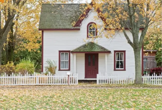 Tree Preservation Planning - Zazueta Tree Specialists - Zazueta Tree Specialists Two-story white house with red trim surrounded by mature trees and autumn foliage.