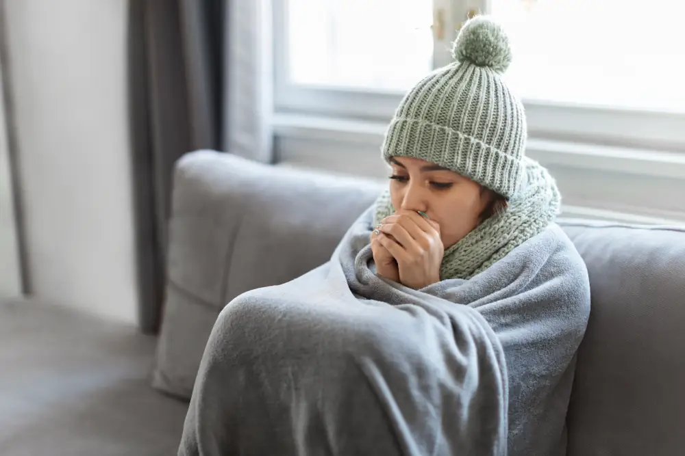 Getting cold air from heating, causes and fixes - Young Woman Feeling Cold At Home, Sitting On Couch Covered In Blanket