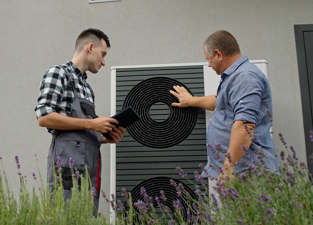 Technician inspecting an outdoor heat pump unit with a homeowner.