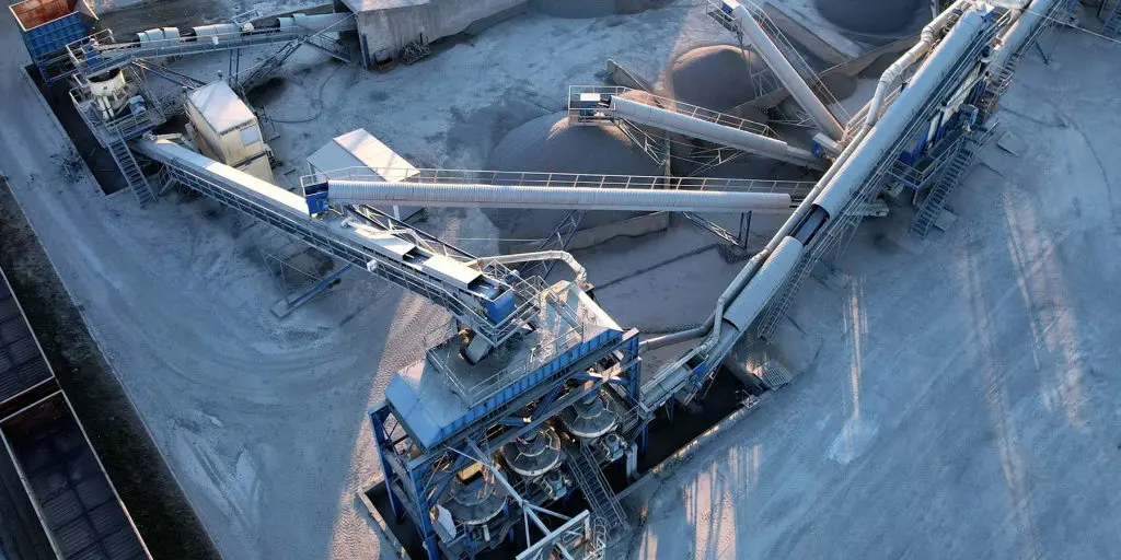 Aerial view of an industrial processing plant with intertwined conveyor belts and metal platforms on a dusty yard.