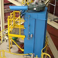 Blue industrial machine with yellow safety stairs and railing in a factory setting.