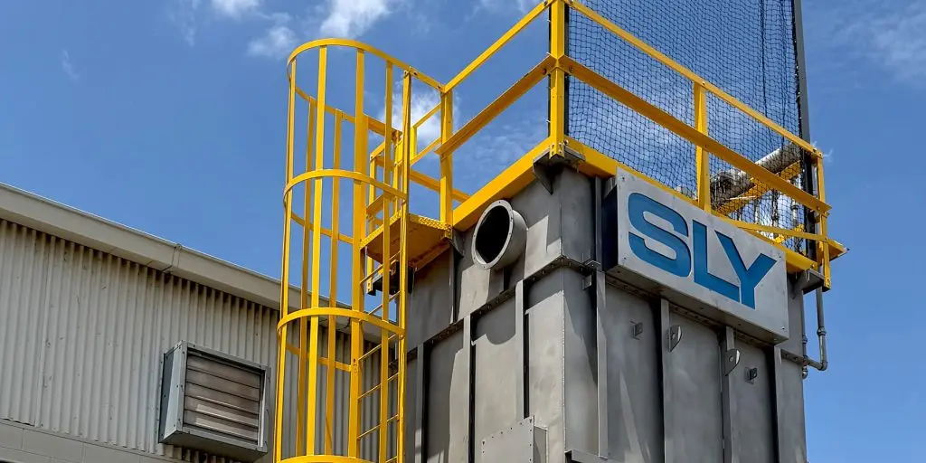 Yellow spiral staircase and safety railing on a gray industrial structure with a large SLY sign against a blue sky.