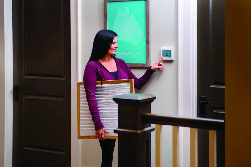 Woman adjusting home thermostat to control HVAC system temperature