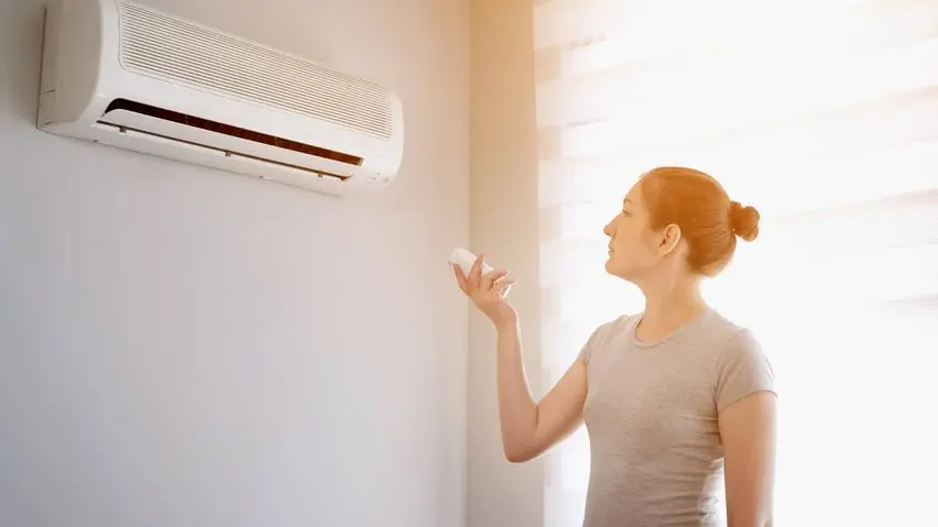 Person adjusting wall-mounted air conditioner with remote control.