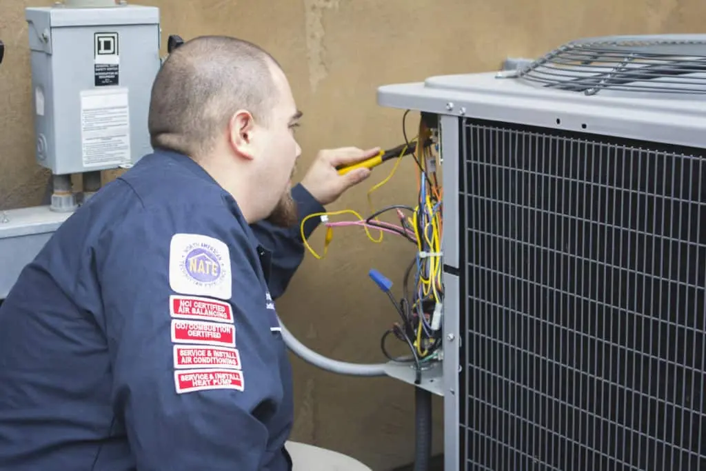 Technician repairing an outdoor air conditioning unit with tools.