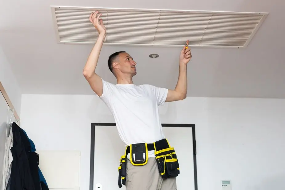Technician adjusting ceiling vent with a screwdriver, wearing a tool belt.