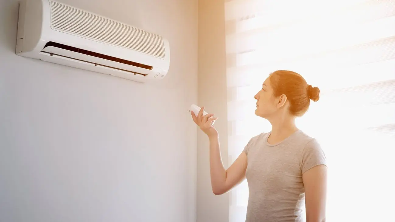 Person adjusting wall-mounted air conditioner with remote control.