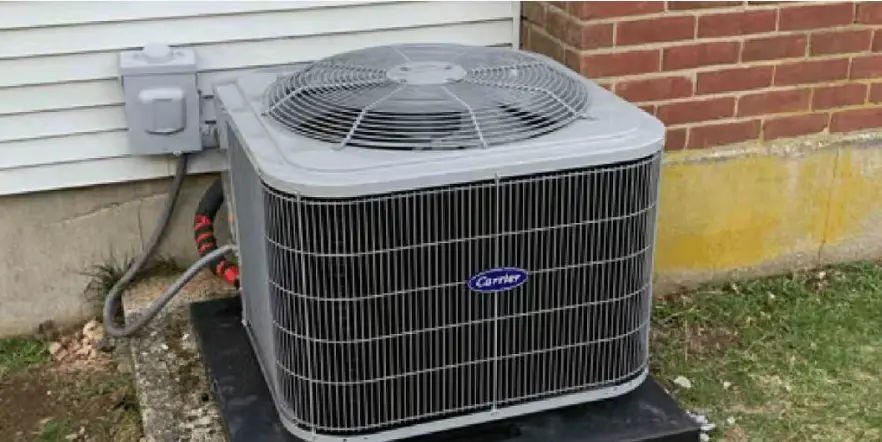 Outdoor air conditioning unit installed on a concrete slab next to a brick wall.