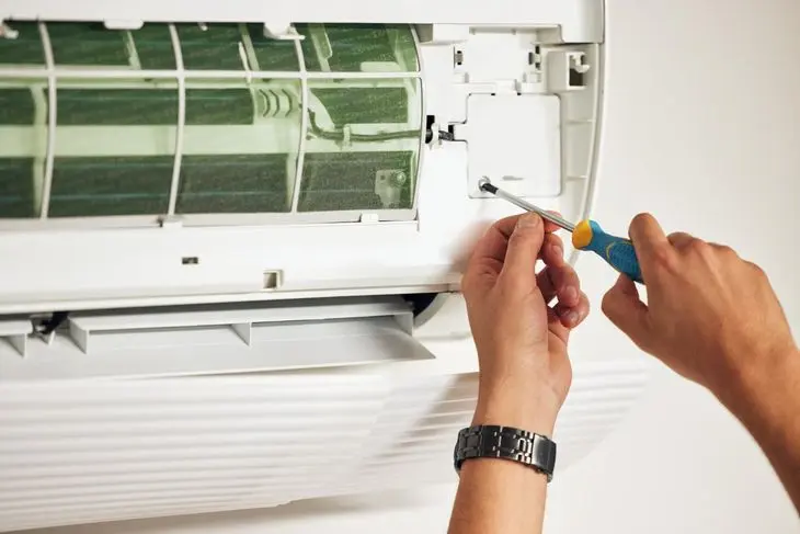 Hands using a screwdriver to repair an air conditioning unit.
