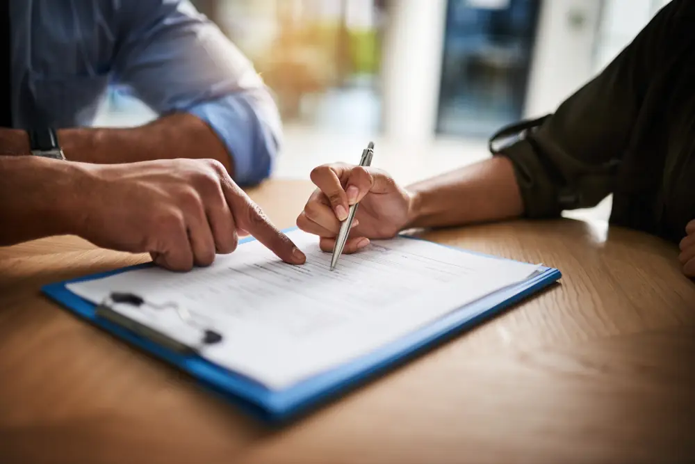 Two people reviewing and signing a document on a table with a pen.
