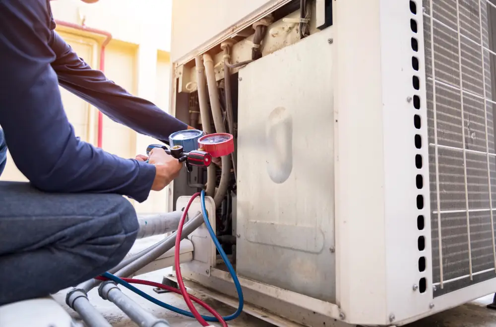Technician using a manifold gauge on an outdoor HVAC unit