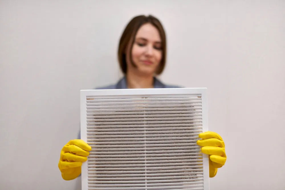 Woman holding a dusty air filter, wearing yellow rubber gloves.
