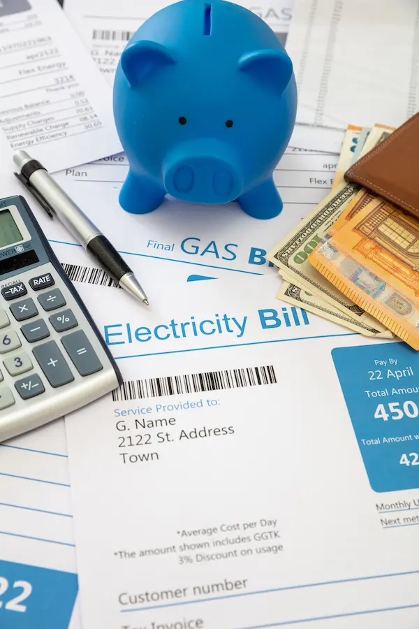 Blue piggy bank on utility bills with calculator, pen, and wallet filled with cash.