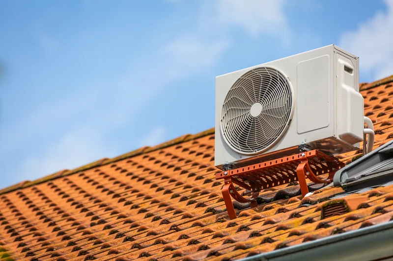 Outdoor air conditioning unit mounted on a red tile roof under a clear blue sky.
