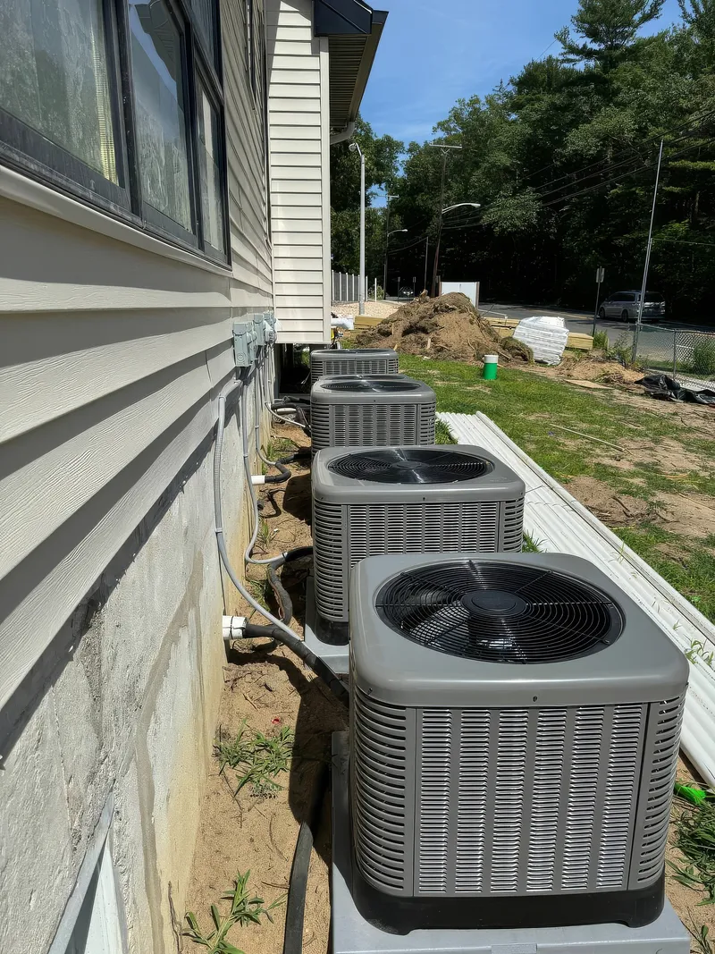 Four outdoor air conditioning units installed beside a house with beige siding.