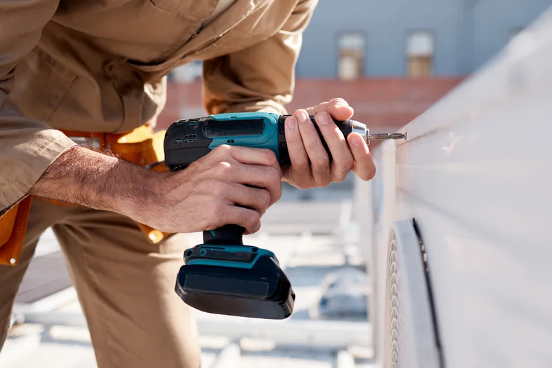 Technician using a cordless drill on an outdoor unit.