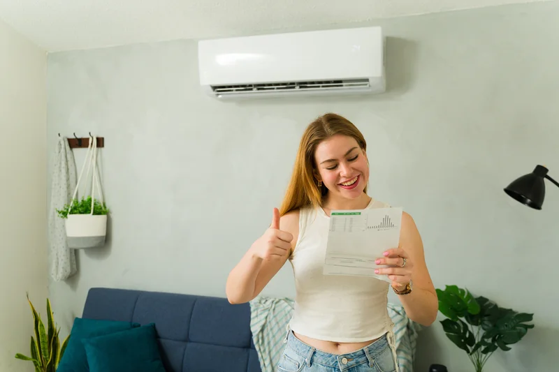 Woman smiling and giving a thumbs up while looking at a document with an air conditioner on the wall in the background.