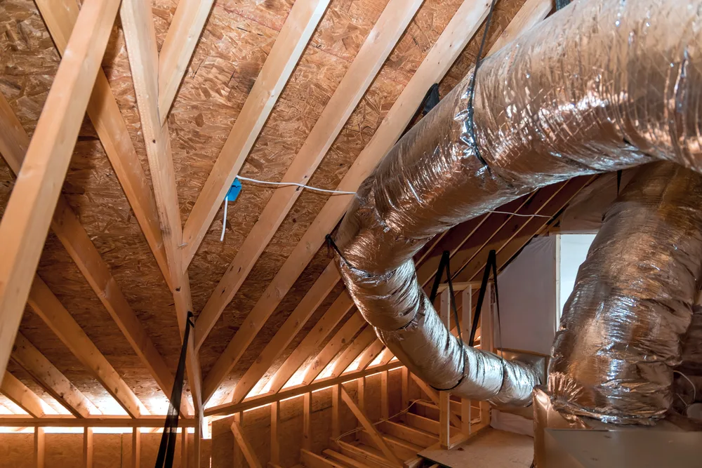 Attic with exposed wooden beams and flexible HVAC ducts installed along the ceiling.