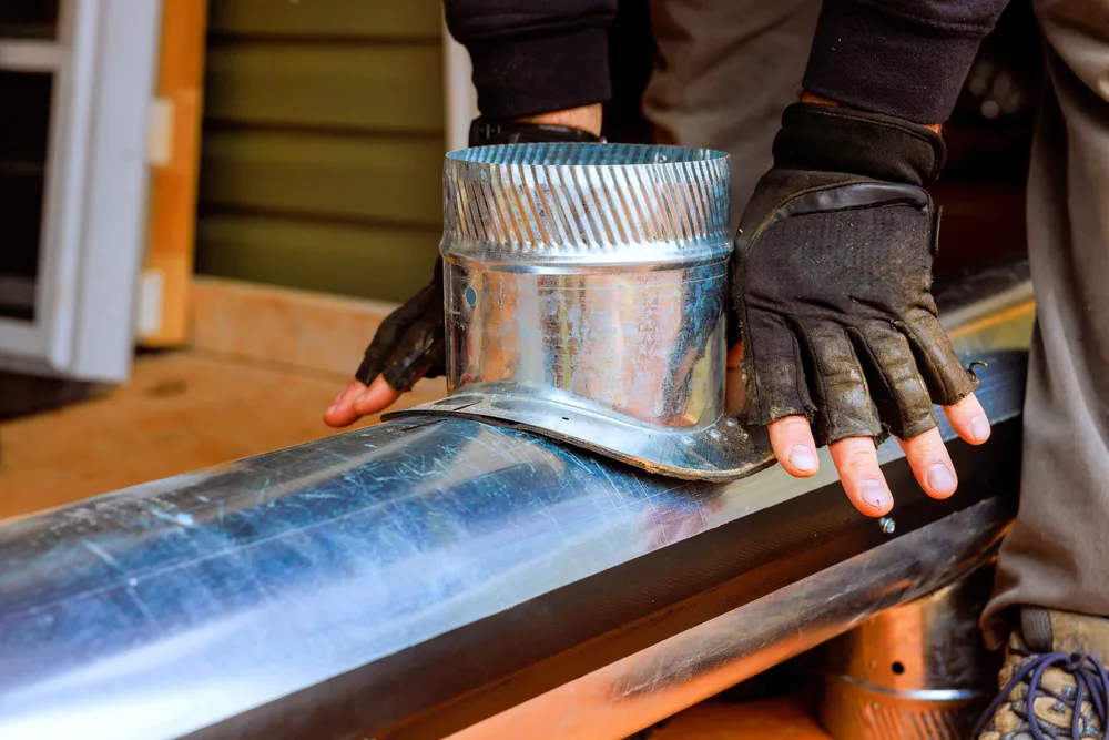 Technician wearing gloves installing metal ductwork on a building exterior.