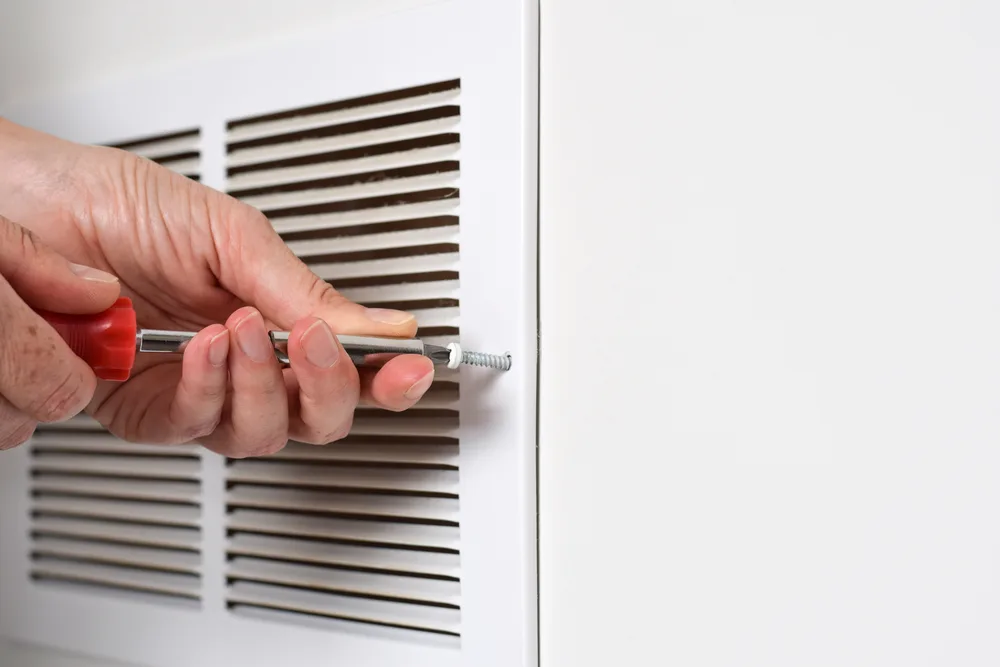 Hand using a screwdriver to fasten a screw on a white vent cover.