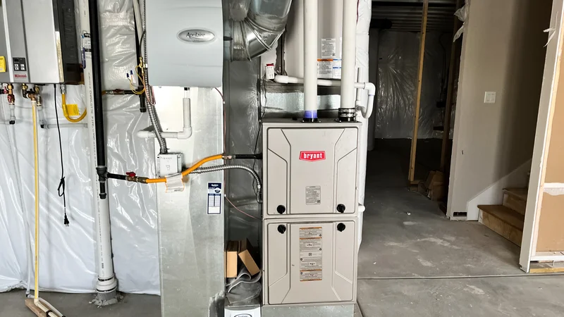 Indoor HVAC system in a basement with pipes, ducts, and a furnace unit.