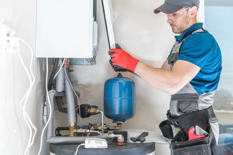 Technician working on a heating system with red gloves and a tool belt.