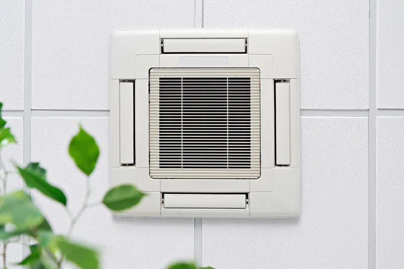 White ceiling air conditioning unit with green leaves in the foreground.
