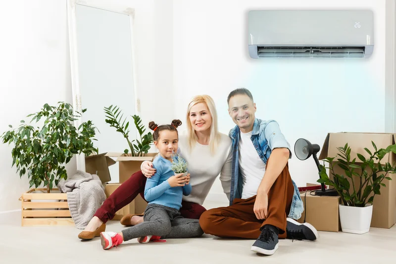 Family sitting on the floor surrounded by plants and boxes, with an air conditioner mounted on the wall.