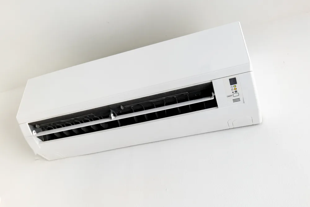 Wall-mounted white air conditioning unit with black vents and control panel.