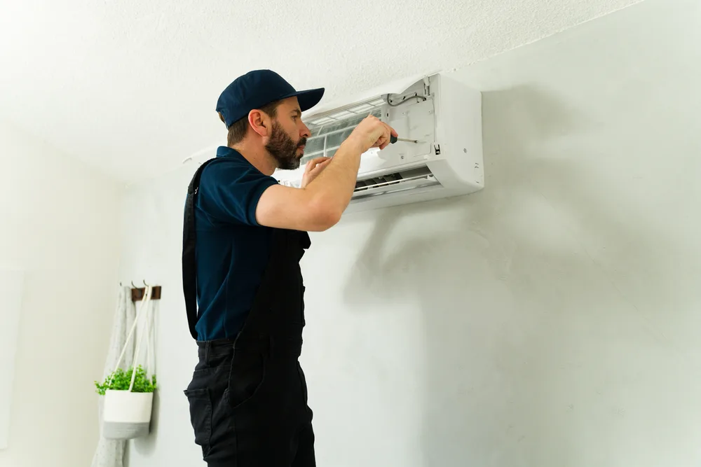 Technician fixing an air conditioning unit on a wall.