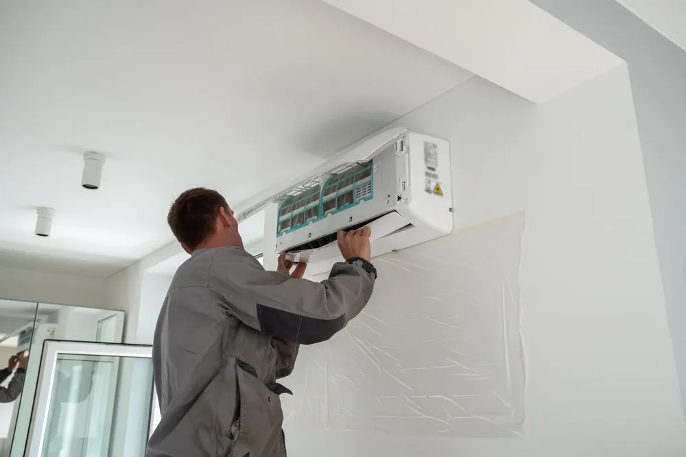Technician in grey uniform working on a wall-mounted air conditioning unit.