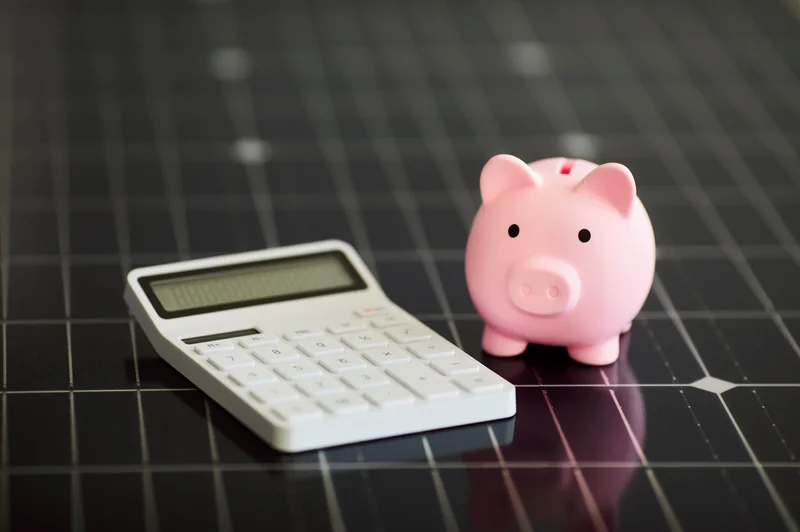 Calculator and pink piggy bank on a dark tile surface.