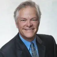 Smiling man in a suit and tie posing for a professional headshot against a light background.
