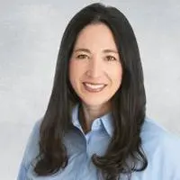 Smiling woman with long dark hair wearing a light blue button-up shirt, posing for a professional headshot.