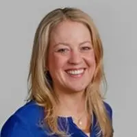 Smiling woman with blonde hair wearing a blue blouse, posing for a professional headshot against a light background.