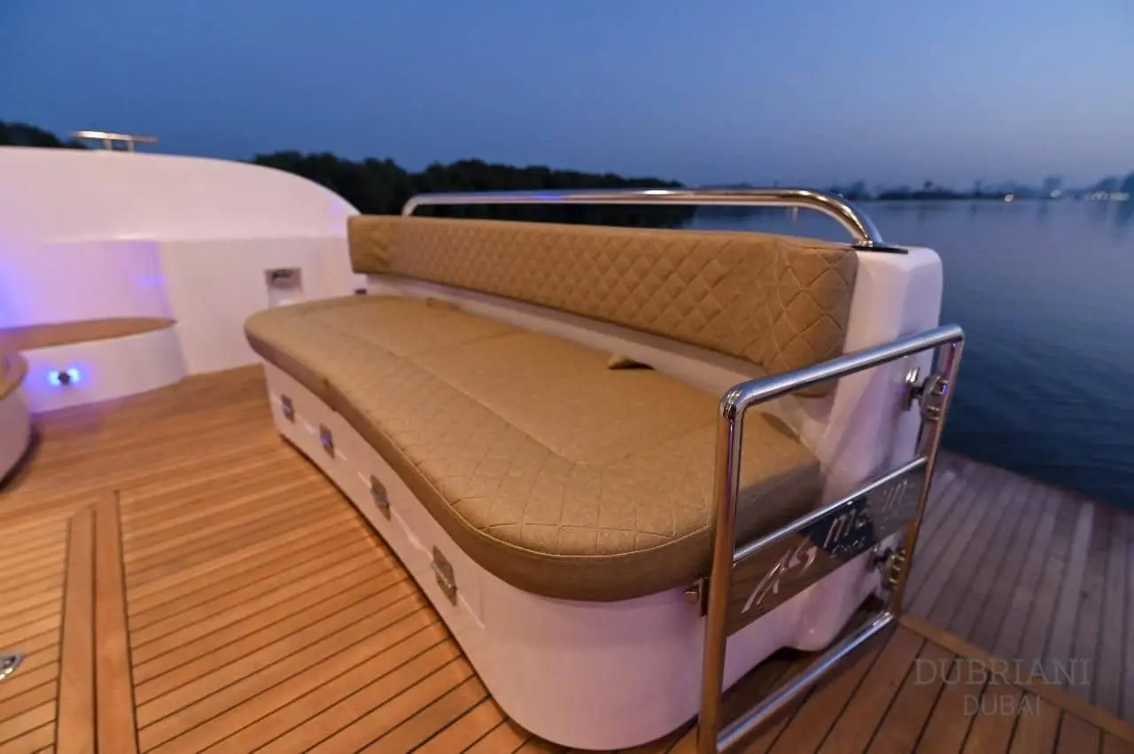 Curved beige aft deck sofa on the Novia 55 at dusk with stainless railing and blue accent lighting