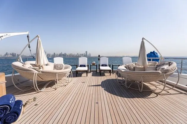 Teak sun deck with round hanging chairs, white loungers and a distant skyline across the water