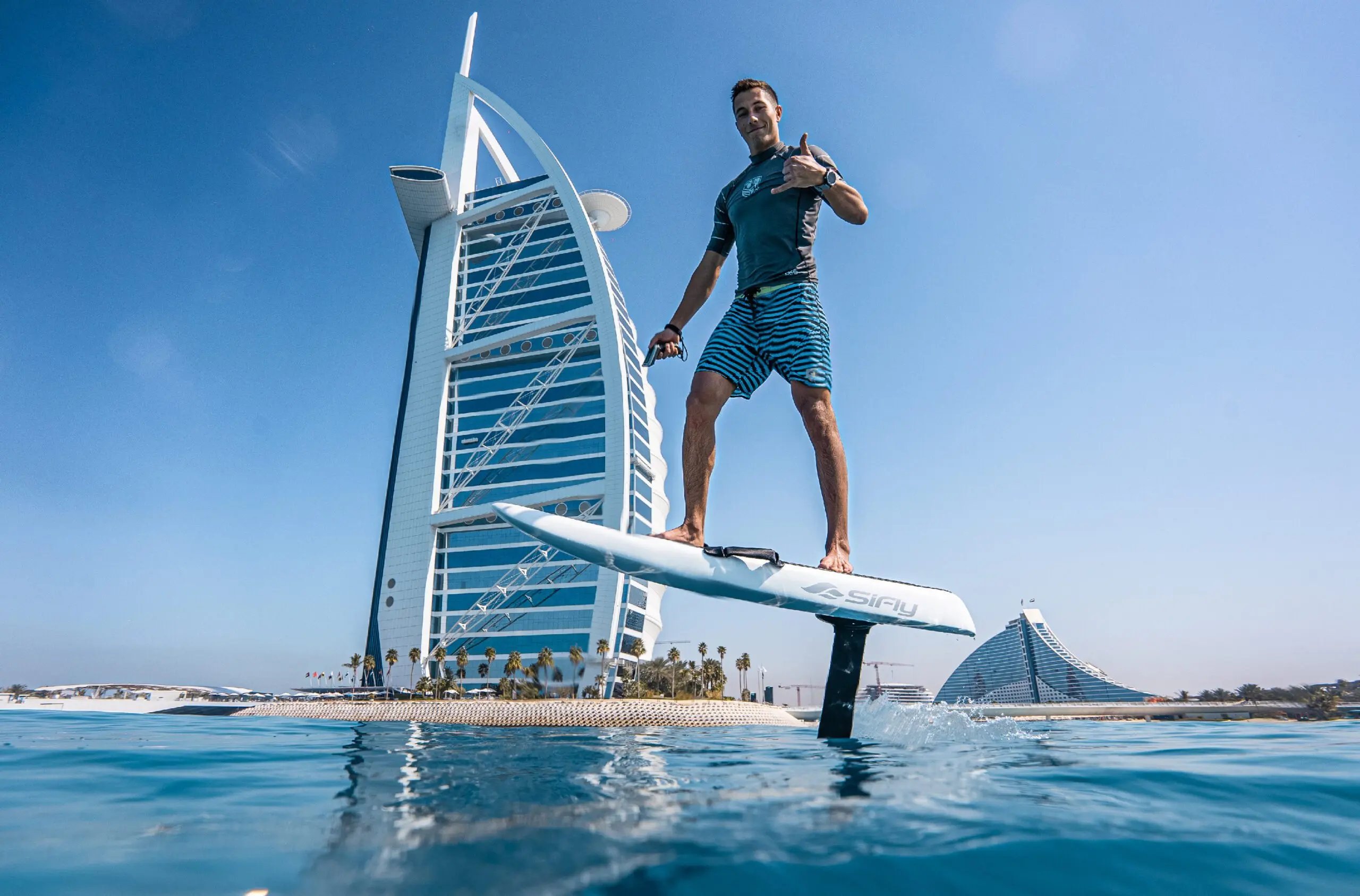 eFoil rider gliding above calm water in front of the sail-shaped Burj Al Arab in Dubai