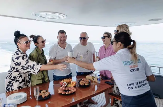 Guests toasting champagne with Dubriani Dubai crew aboard a luxury yacht at sea.