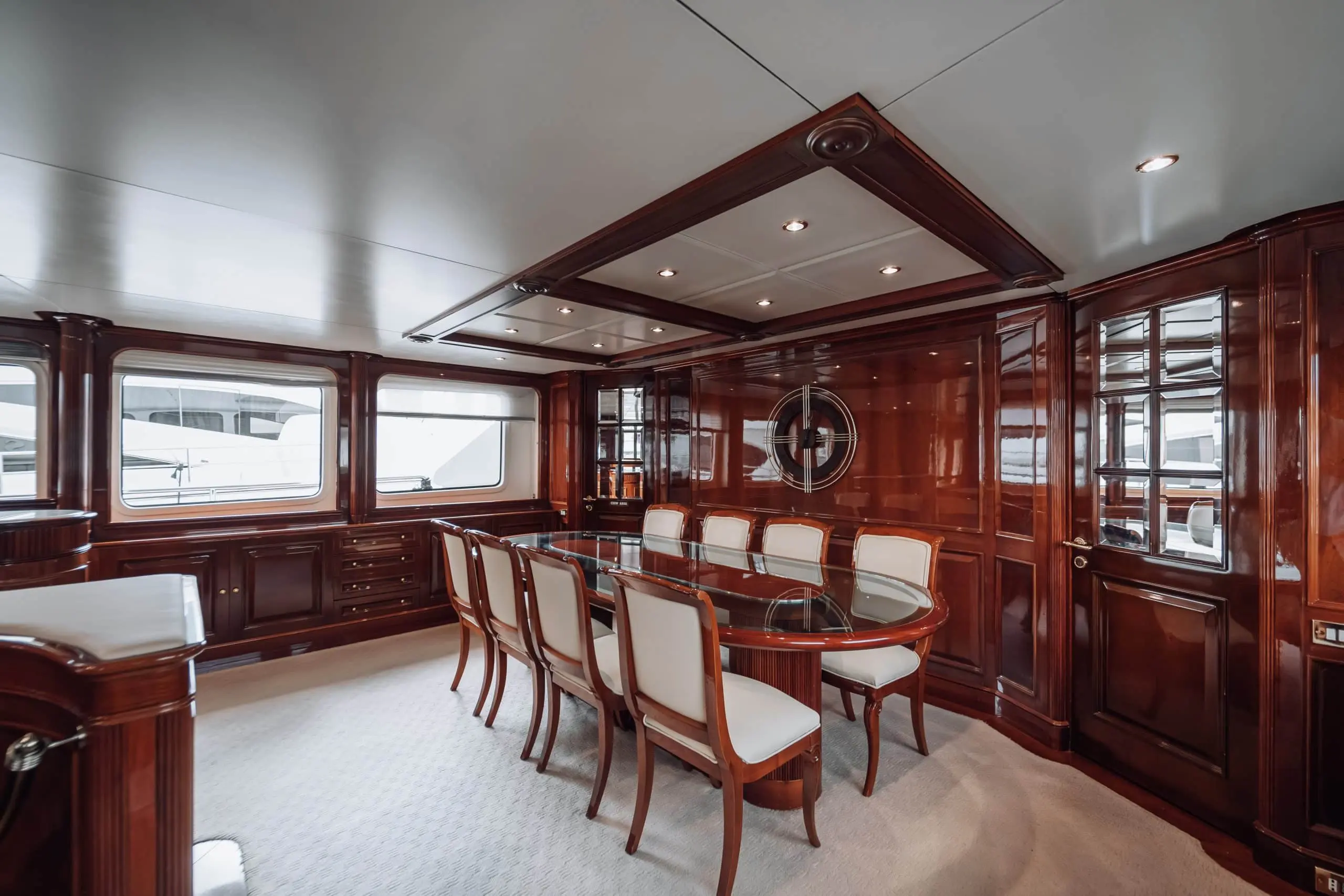 Luxury yacht dining room with polished wooden interiors and elegant glass table.