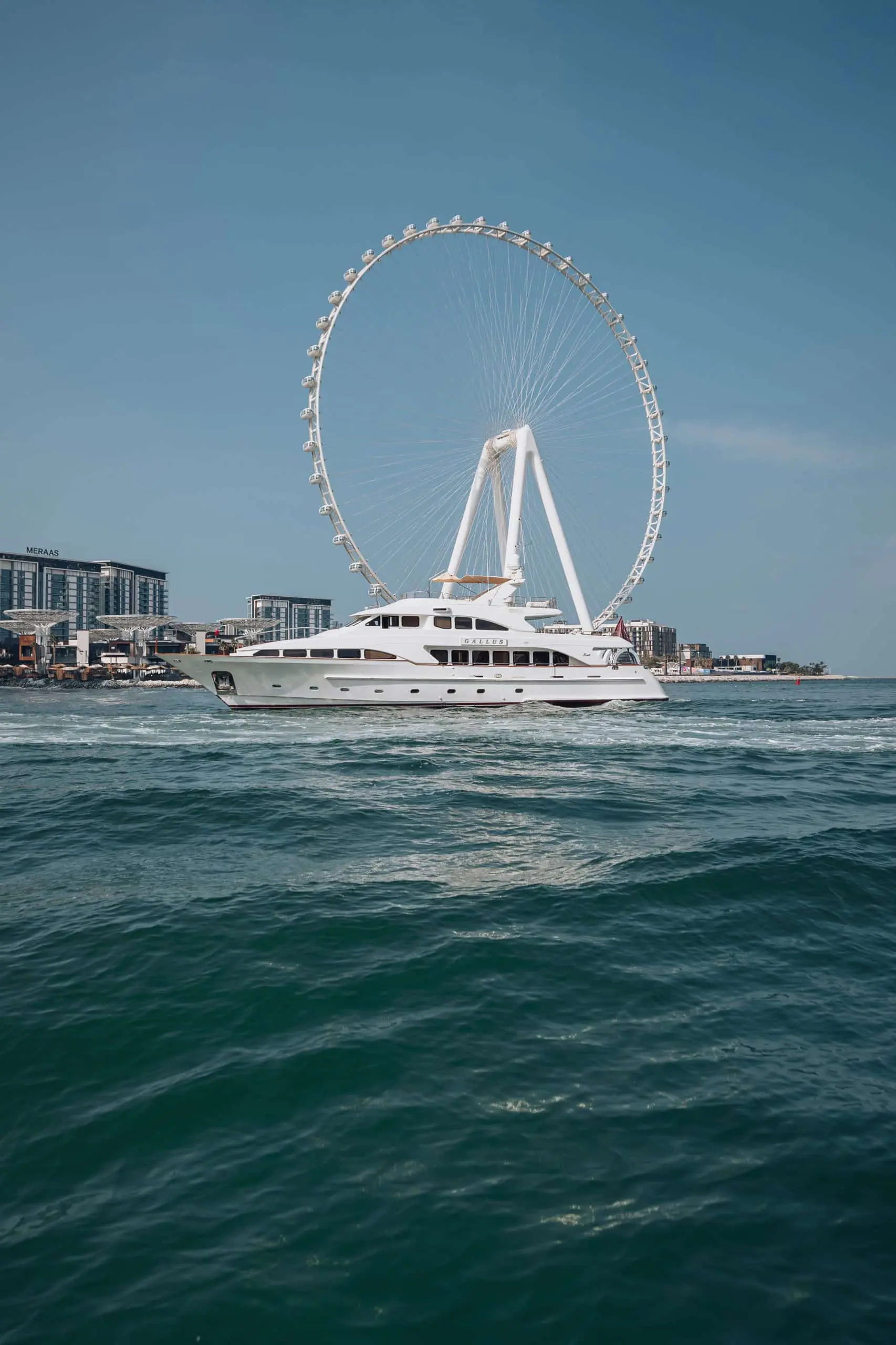 Luxury yacht cruising on blue waters with Ain Dubai towering in the background, Dubai skyline visible on a clear sunny day.