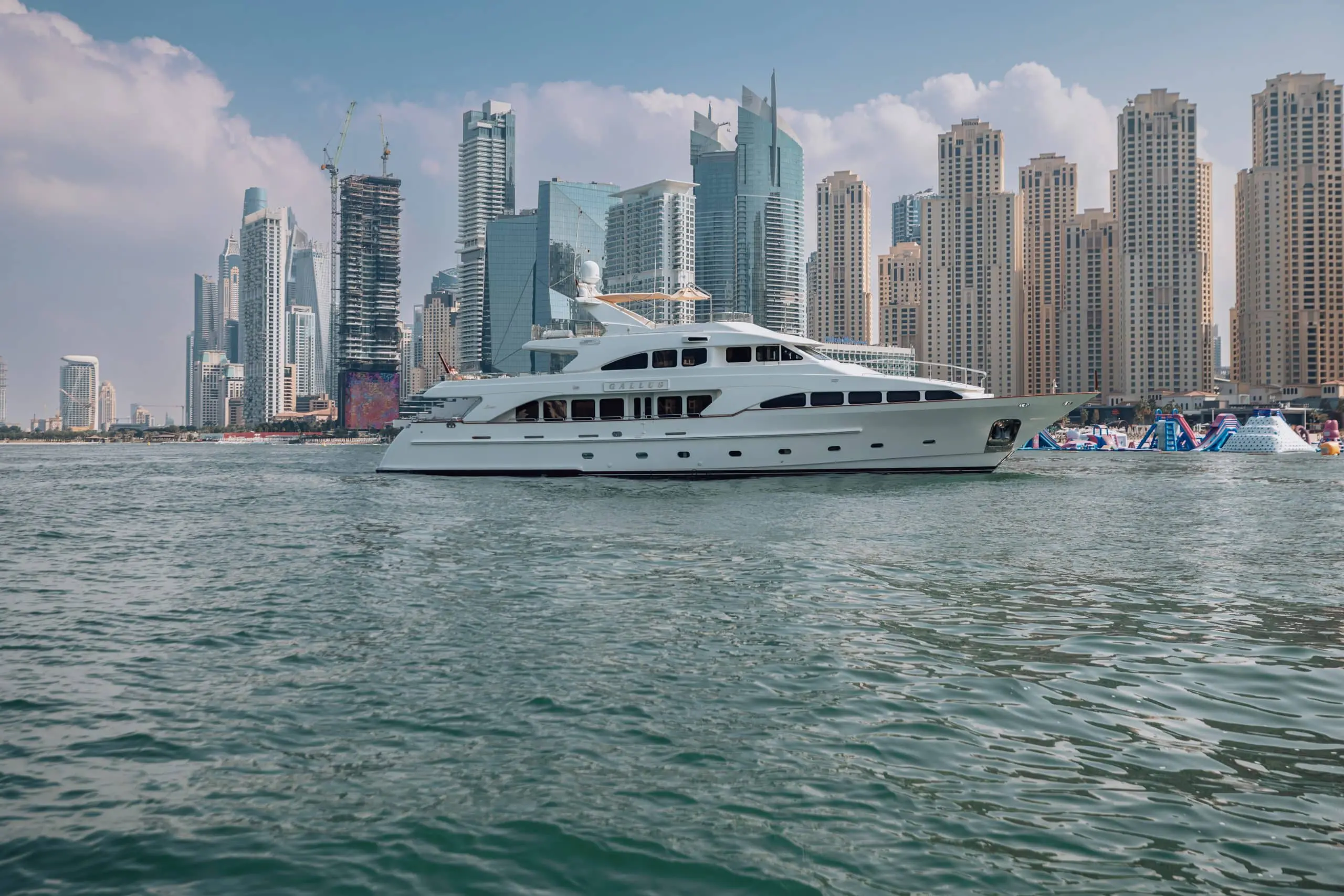 Luxury white yacht cruising along the waterfront of Dubai Marina with the modern skyline of Dubai in the background on a sunny day