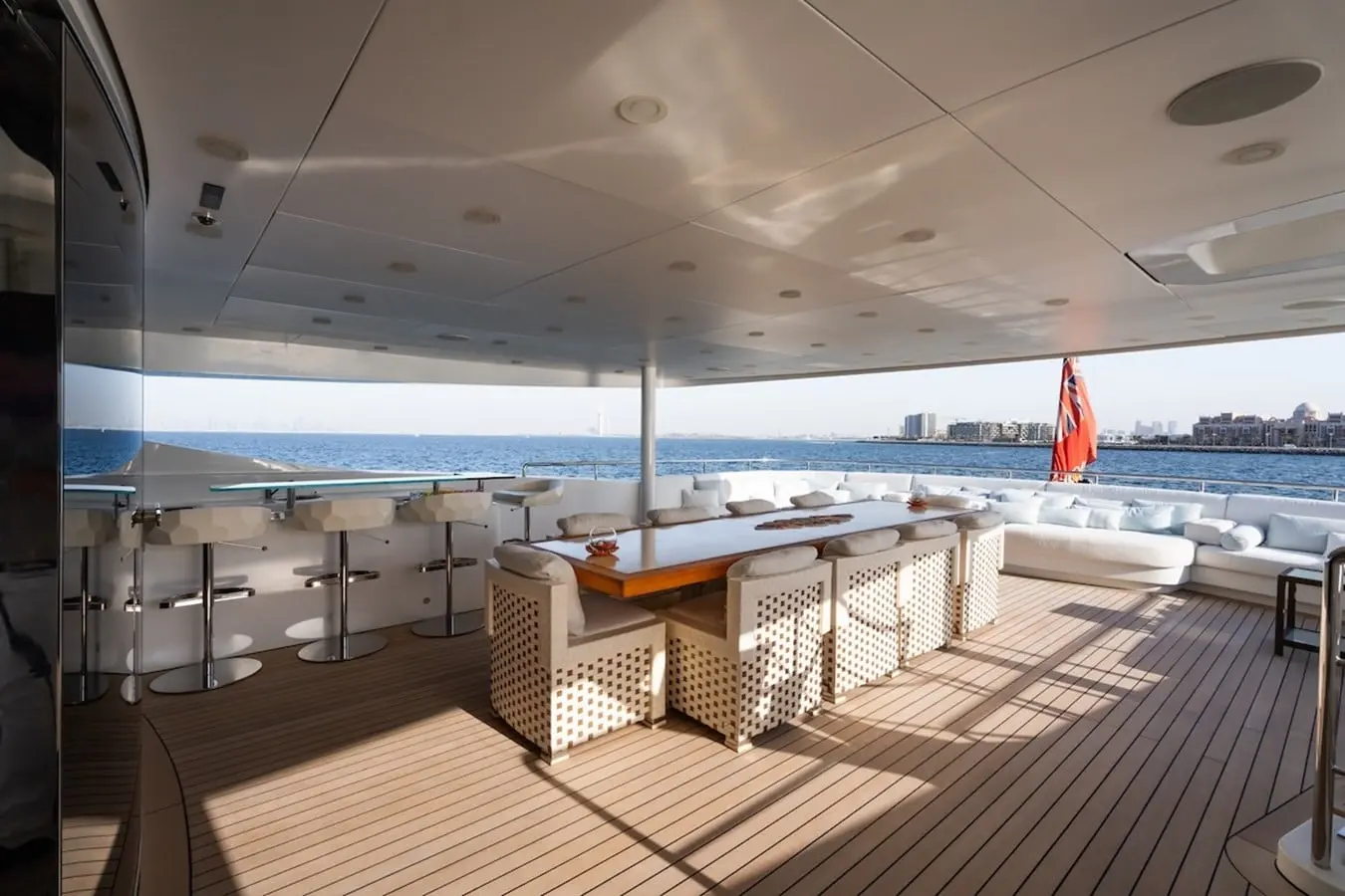 Shaded teak aft deck of the 54m Baglietto with alfresco dining table, bar stools and sofa seating