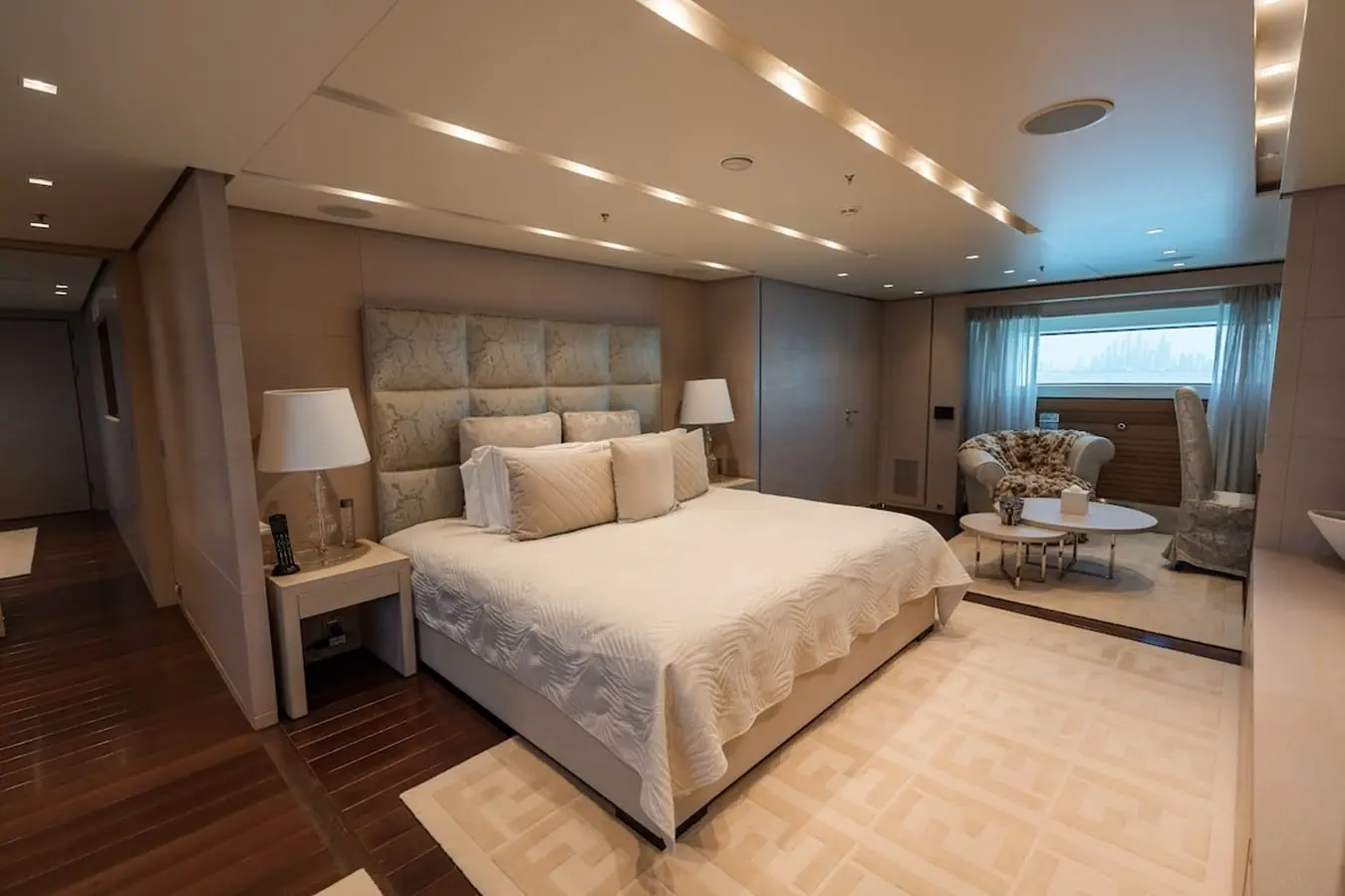 Yacht master stateroom with king bed, tufted headboard and a window seating area with armchairs