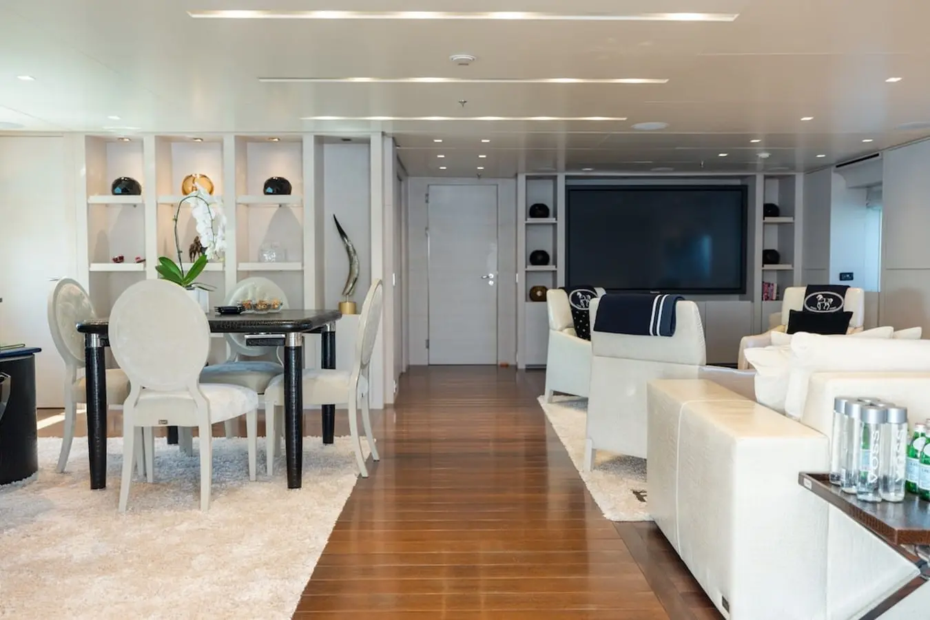 Yacht main salon with white sofas facing a wall-mounted TV and a dining table with white chairs