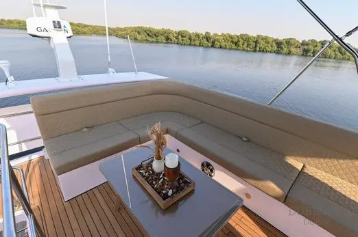 Alfresco deck seating on the Novia 55 with a wraparound beige sofa, dining table and drinks tray