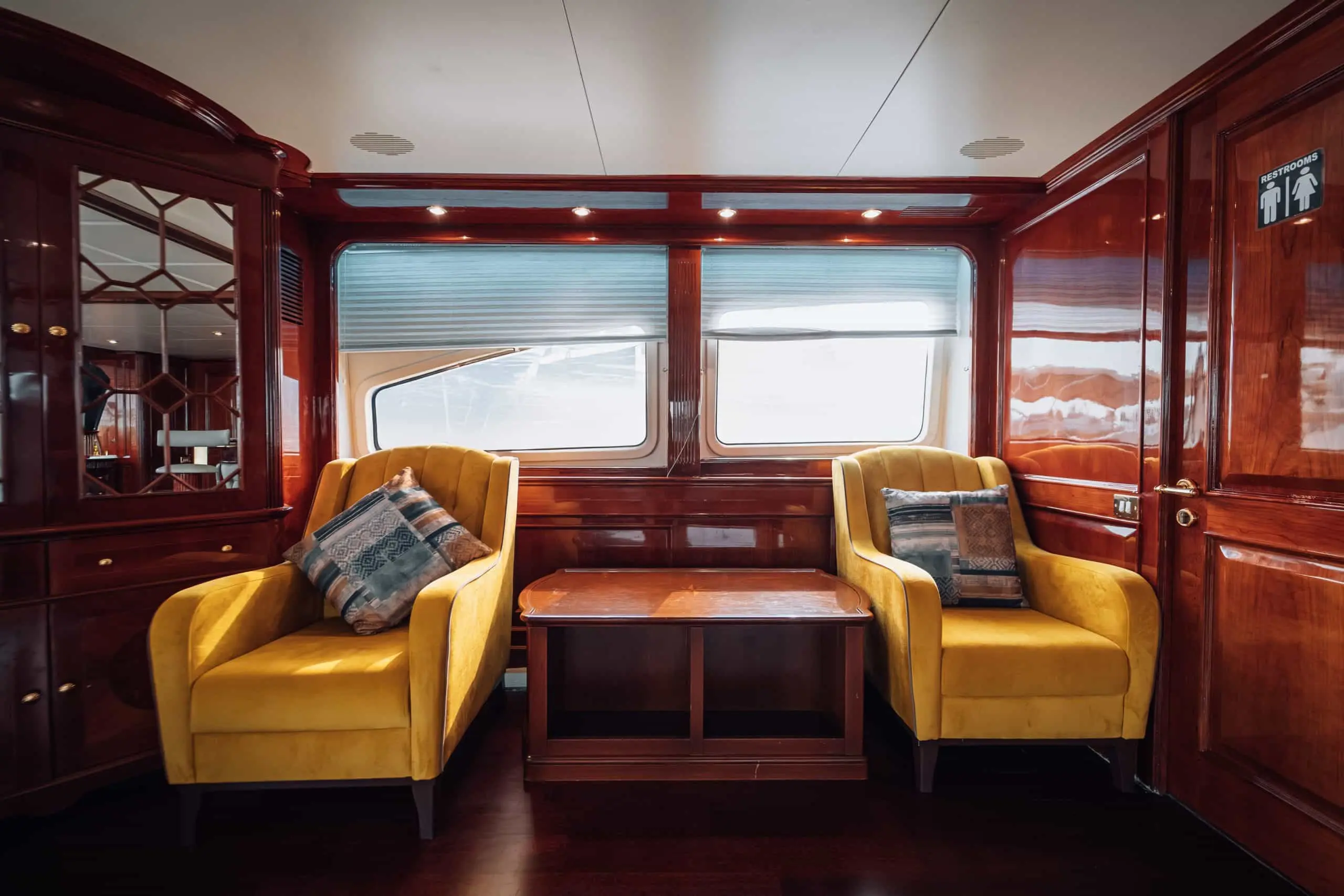 Luxury yacht seating area with wooden interiors and comfortable armchairs by sea-view windows.