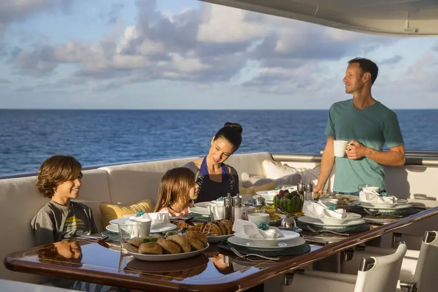 Family sharing a meal at a laid table on a yacht's aft deck with open sea behind