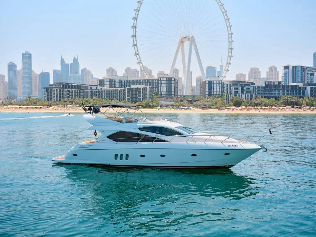 White luxury yacht cruising on calm turquoise water with a large observation wheel and modern city skyline in the background.