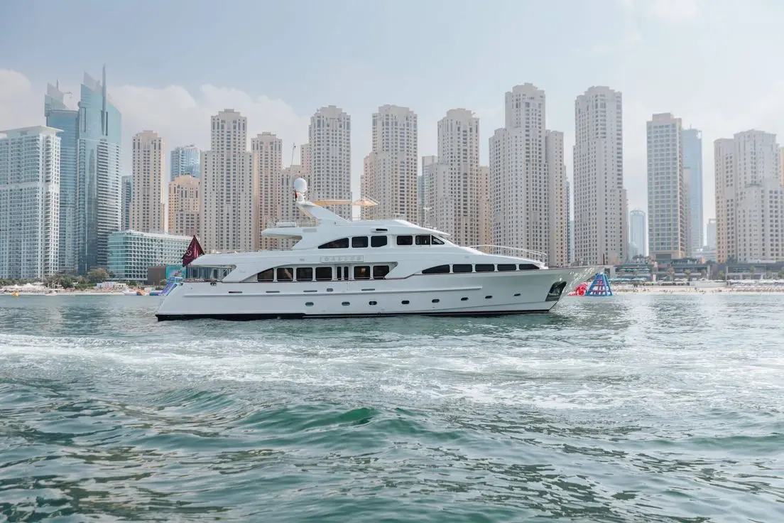 Luxury yacht cruising along the coastline of Dubai Marina, Dubai with high-rise skyline in the background.